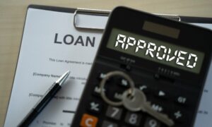 Paper with loan on it and a calculator with the word approved