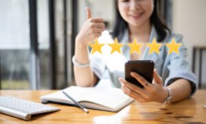 Young woman at her desk looking at her phone and making a thumbs-up sign because she has received a 5 star review for her pet sitting business